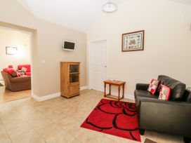 A small sitting area with a black leather sofa with cushions a red rug a wooden cabinet and a small table at 2 Pines Farm Cottages Ulleskelf