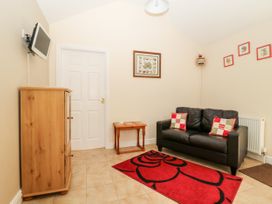 A small sitting room with a black sofa two cushions a red rug a wooden cabinet a wall-mounted TV and framed pictures at 2 Pines Farm Cottages Ulleskelf