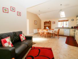 An open plan room with a black sofa and red pillows a dining table with wooden chairs and kitchen cabinets in 2 Pines Farm Cottages Ulleskelf