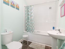 A bathroom with a toilet, bathtub with shower curtain, sink, small stool, and wall art at 2 Pines Farm Cottages in Ulleskelf