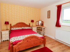 A bedroom with a wooden bed red bedding bedside tables with red lamps a dressing table with a mirror and stool and a window with red curtains at 2 Pines Farm Cottages Ulleskelf