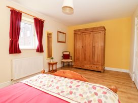 A bedroom with a wooden wardrobe a chair a small table with a plant a window with red curtains and a bed with a colorful duvet at 2 Pines Farm Cottages Ulleskelf