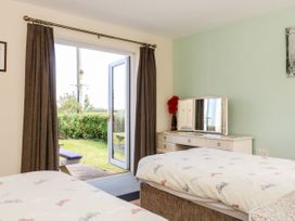 A bedroom with two beds a dressing table with a mirror and a vase with red flowers and an open door leading outside at 2 Pines Farm Cottages in Ulleskelf