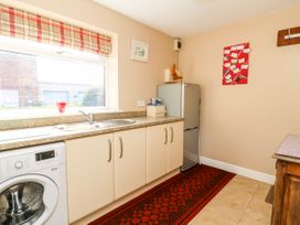 A kitchen with a washing machine, sink, refrigerator, countertop, red patterned rug, window with a plaid blind, and decorations on the walls at 2 Pines Farm Cottages Ulleskelf