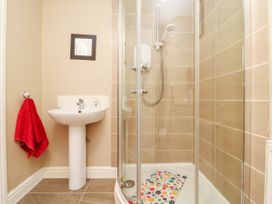 A bathroom with a pedestal sink a red towel on a hook a glass shower enclosure and a colorful bath mat at 2 Pines Farm Cottages Ulleskelf