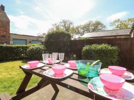 An outdoor picnic table set with pink bowls, floral plates, clear glasses and a green bowl in a garden at 2 Pines Farm Cottages Ulleskelf