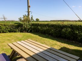 An outdoor picnic table on a grassy lawn with a hedge and open fields with sheep in the background at 2 Pines Farm Cottages in Ulleskelf