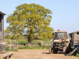 A tractor parked near farm buildings with a large tree and green field in the background at 2 Pines Farm Cottages in Ulleskelf