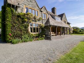A stone house with ivy on the walls a covered porch with wooden chairs and a gravel driveway at Plas Gwynfryn in Llanbedr