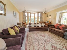 A living room with three sofas a patterned rug armchairs and a large bay window at Plas Gwynfryn in Llanbedr