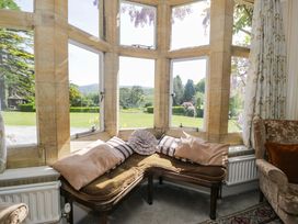 A corner seating area with cushions by large stone-framed windows overlooking a garden at Plas Gwynfryn in Llanbedr