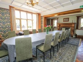 A dining room with a long table and green chairs a vase with flowers on the table a fireplace and large windows at Plas Gwynfryn in Llanbedr