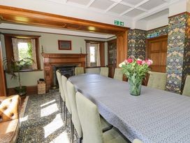A dining room with a long table covered by a patterned tablecloth and chairs around it at Plas Gwynfryn in Llanbedr