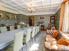 A dining room with a long table covered with a cloth surrounded by chairs and a leather sofa near the window at Plas Gwynfryn in Llanbedr
