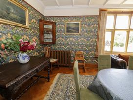 A dining room with a wooden table vase of flowers patterned wallpaper and framed paintings at Plas Gwynfryn in Llanbedr