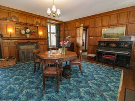A dining room with wooden paneling a table with chairs a fireplace and a piano at Plas Gwynfryn in Llanbedr