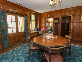A dining room with a wooden table set with flowers and tea near wooden doors at Plas Gwynfryn in Llanbedr