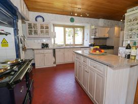 A kitchen with white cabinets a center island with fruit plates bottles of wine and glasses a stove and a window at Plas Gwynfryn in Llanbedr