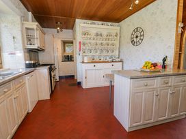A kitchen with cream cabinets a countertop island a dish rack with plates and cups and a wall clock at Plas Gwynfryn in Llanbedr