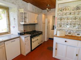 A kitchen with a gas stove dishwasher refrigerator and a cabinet with floral plates and cups at Plas Gwynfryn in Llanbedr