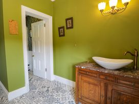 A bathroom with a green wall, a wooden vanity with a white vessel sink and brass faucet, patterned tile floor, and a white door leading to another room at Plas Gwynfryn in Llanbedr