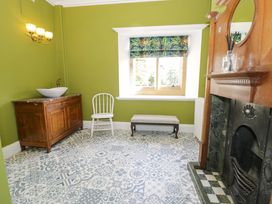 A room with green walls decorative tiled floor wooden cabinet with sink white chair bench window with patterned blind and fireplace at Plas Gwynfryn in Llanbedr
