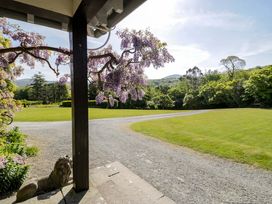 A gravel driveway curving through a lawn with trees and flowers near a porch at Plas Gwynfryn in Llanbedr