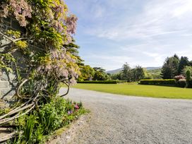 A gravel path near a stone wall covered with flowering vines and a garden with lawn and trees in the background at Plas Gwynfryn in Llanbedr