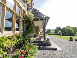 A stone house exterior with climbing plants and patio furniture next to a gravel driveway and garden at Plas Gwynfryn in Llanbedr