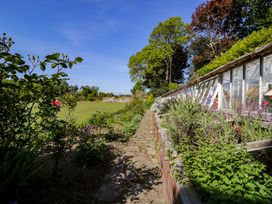 A garden pathway with plants and flowers next to a greenhouse at Plas Gwynfryn in Llanbedr