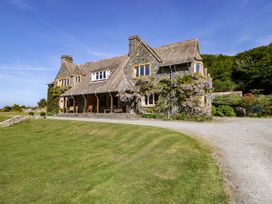 A stone house with a tiled roof surrounded by a lawn and trees at Plas Gwynfryn in Llanbedr