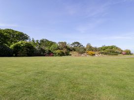 A large grassy lawn with shrubs and trees in the background under a clear sky at Plas Gwynfryn in Llanbedr