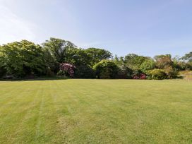 A large grassy lawn with various trees and bushes in the background at Plas Gwynfryn in Llanbedr