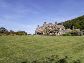A large stone house with multiple chimneys surrounded by a lawn and trees at Plas Gwynfryn in Llanbedr