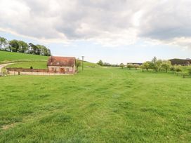 A small brick house with a red roof surrounded by a fenced green field and trees at Shepherd's Barn Between Milborne St Andrew and Winterborne Whitechurch