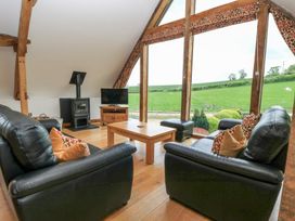 A living room with black leather sofas wooden coffee table wood stove and large windows overlooking a green field at Shepherd's Barn Between Milborne St Andrew and Winterborne Whitechurch