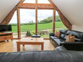 A living room with black leather sofas a wooden coffee table a television and large windows overlooking green fields at Shepherd's Barn Between Milborne St Andrew and Winterborne Whitechurch