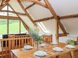 A dining table set with bowls glasses and cutlery near wooden beams and windows showing a green field at Shepherd's Barn Between Milborne St Andrew and Winterborne Whitechurch