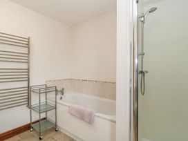 A bathroom with a bathtub towel rack glass shelving unit and a shower at Shepherd's Barn Between Milborne St Andrew and Winterborne Whitechurch