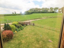 A garden with bushes and grass overlooking fenced green fields and trees at Shepherds Barn Between Milborne St Andrew and Winterborne Whitechurch