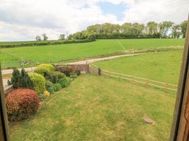 A garden with bushes and a lawn next to a wooden fence and green fields at Shepherds Barn Between Milborne St Andrew and Winterborne Whitechurch