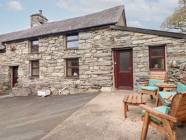 An outdoor seating area with wooden chairs and a small table outside a stone cottage at Y Bwthyn Llanbedr near Harlech