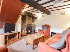 A sitting room with wooden beams a stone fireplace orange armchairs and a wooden coffee table at Y Bwthyn in Llanbedr near Harlech