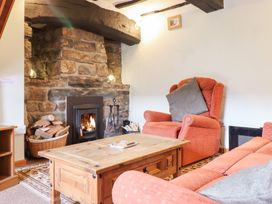 A living room with a wooden coffee table orange armchairs a stone fireplace with a fire and a basket of firewood at Y Bwthyn in Llanbedr near Harlech