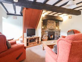 A living room with a stone fireplace a television on a wooden stand and red armchairs at Y Bwthyn in Llanbedr near Harlech