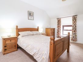 A bedroom with a wooden bed and matching bedside tables with lamps a chest of drawers and patterned curtains at Y Bwthyn in Llanbedr near Harlech