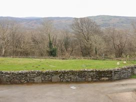A stone wall with a metal gate in front of a green field with sheep and leafless trees at Y Bwthyn in Llanbedr near Harlech
