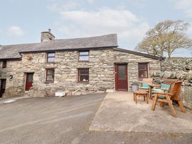 An exterior view of a stone cottage with wooden doors and windows and outdoor wooden seating at Y Bwthyn in Llanbedr near Harlech