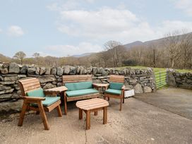 An outdoor seating area with wooden chairs and table on a concrete surface near a stone wall at Y Bwthyn in Llanbedr near Harlech
