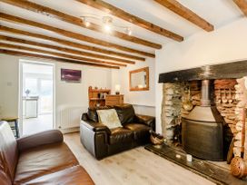 A living room with two leather sofas a stone fireplace wooden beams on the ceiling and a wooden cabinet at 3 Tyn Y Mynydd in Penmachno